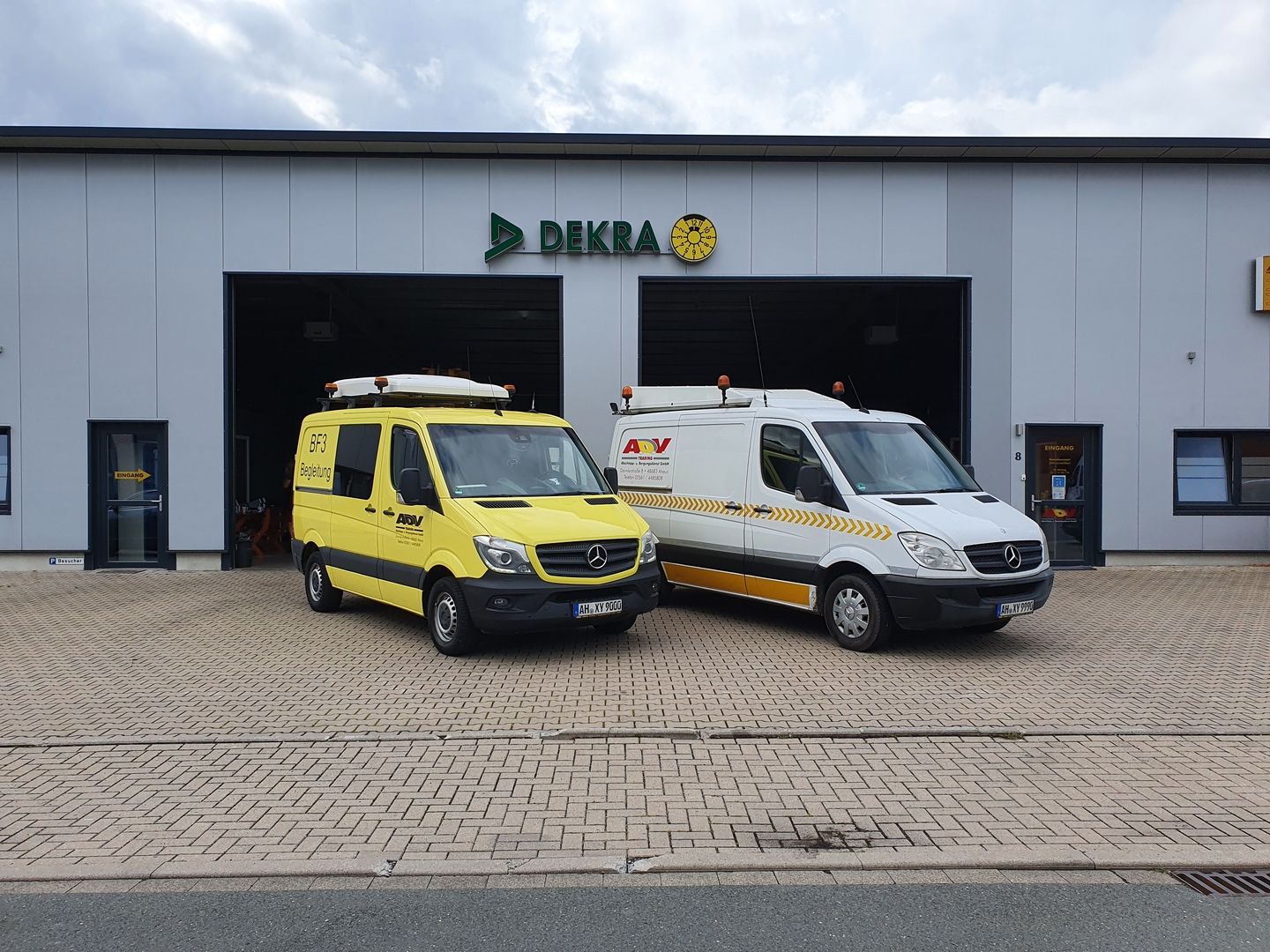 Zwei Mercedes-Transporter vor einem DEKRA-Gebäude, ein gelber und ein weiß gestreifter